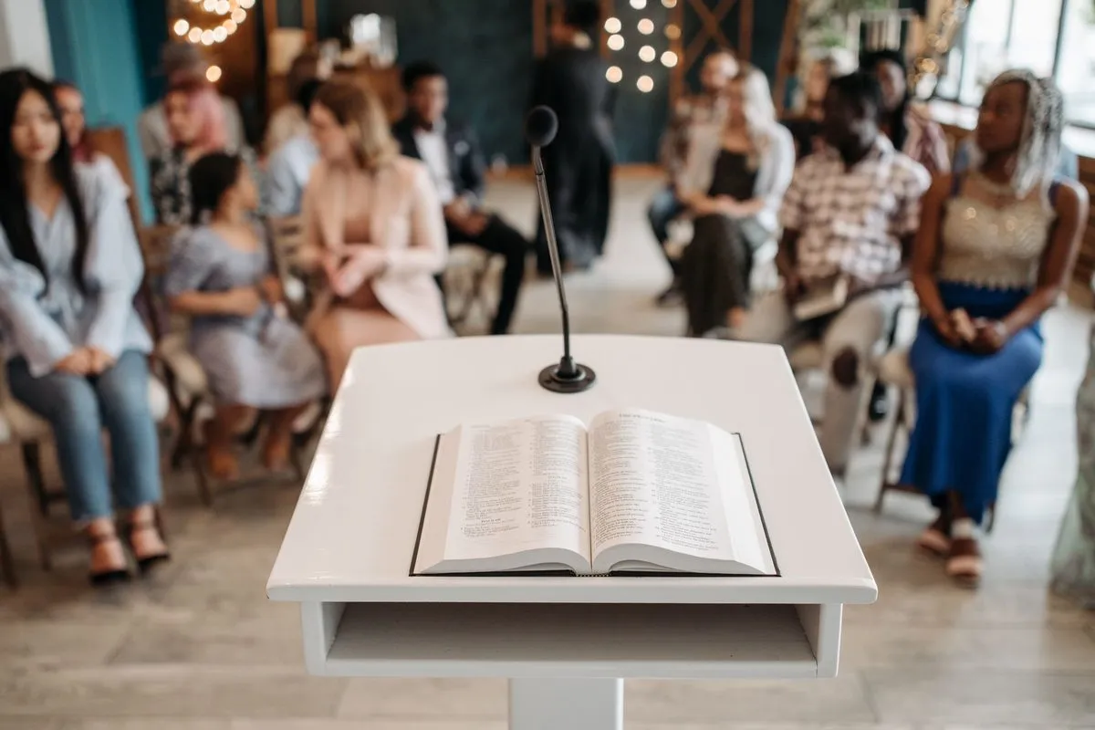 An open Bible on a white lectern, with people seated in rows behind it
