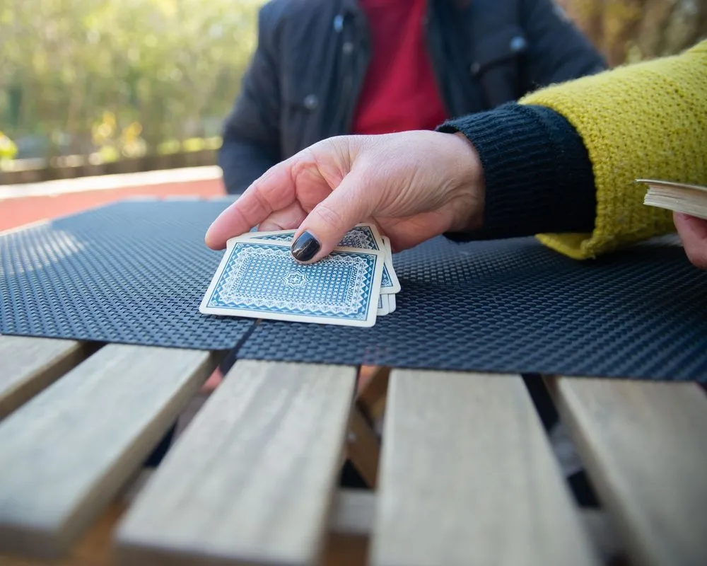 A hand laying down playing cards on an outdoor table